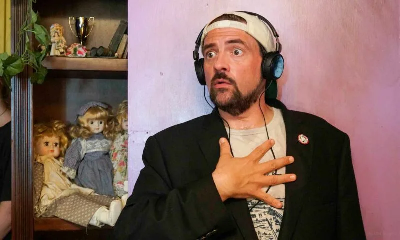 Kevin Smith in headphones on set, surrounded by shelves of dolls