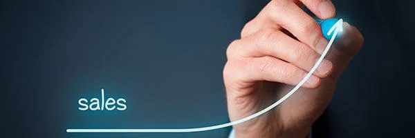 A hand draws a glowing white line curving steeply upward from the word "sales" on a dark background.