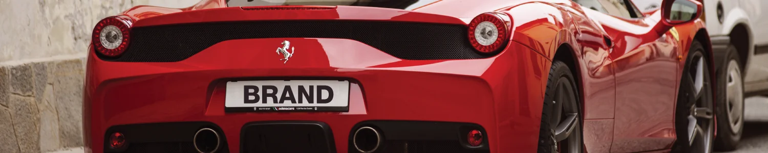 Rear of a red sports car with a plate reading BRAND, parked by a stone wall.