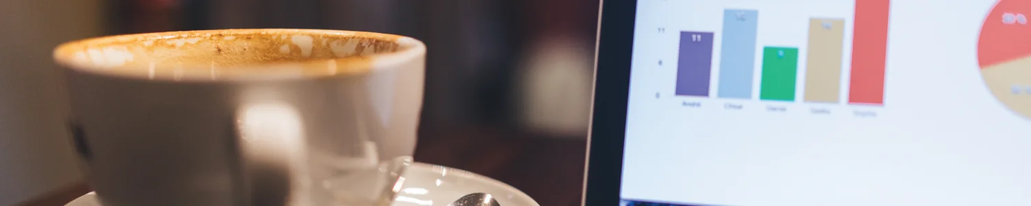 A used cappuccino cup on a saucer beside a laptop screen showing a colourful bar chart and pie chart.