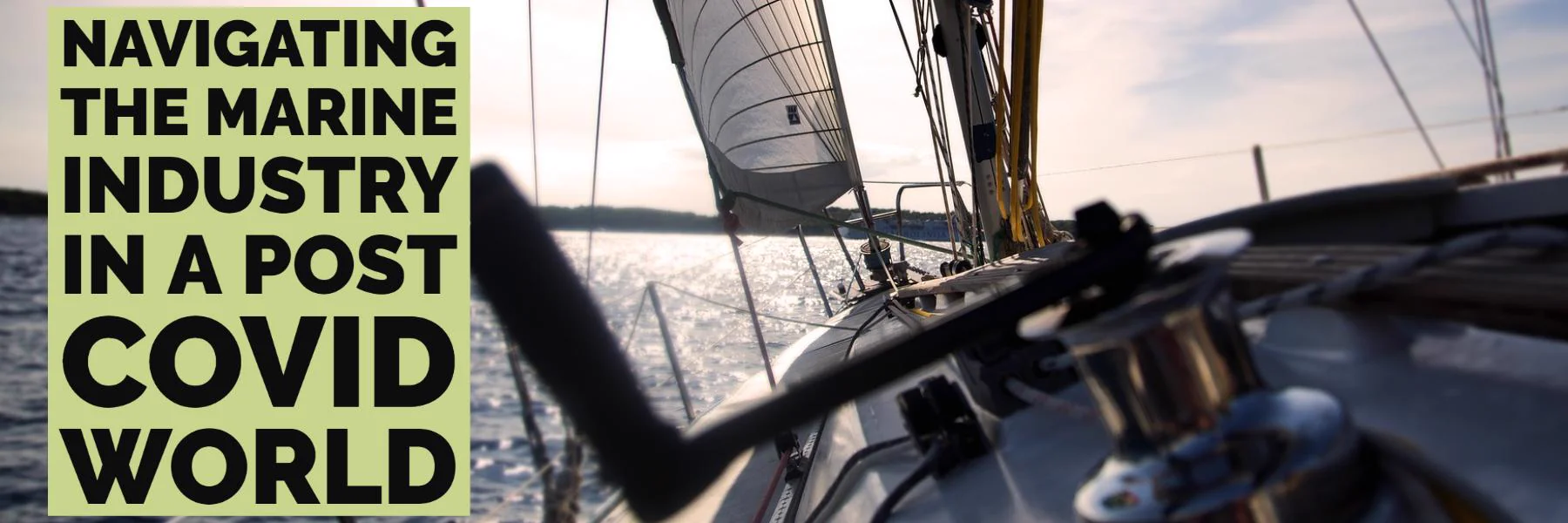 Sailboat deck with a winch handle in the foreground, a white sail above, and sunlit water behind.