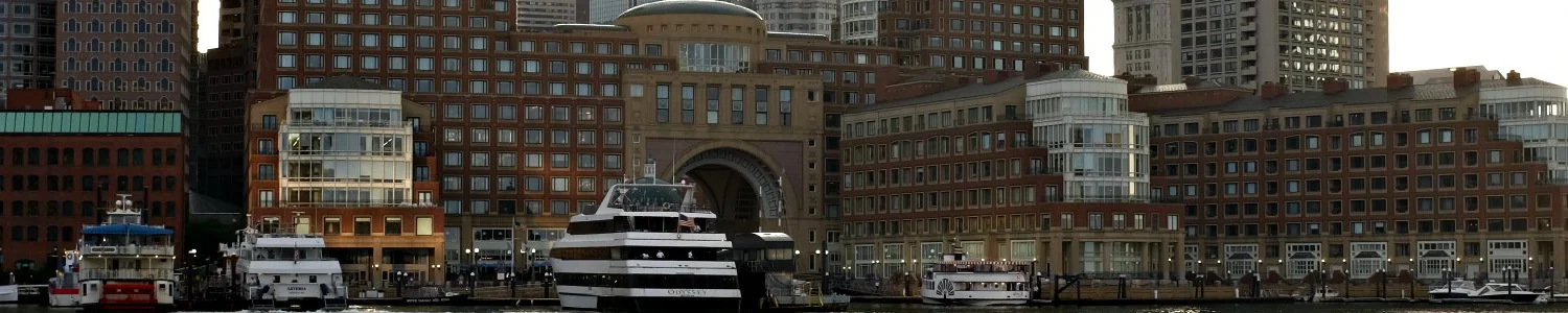 Tour boats docked at a waterfront lined with large red-brick buildings, including one with a central arched entrance.