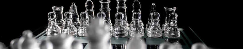 Glass chess pieces lined up on a glass board against a black background, with pawns in front.