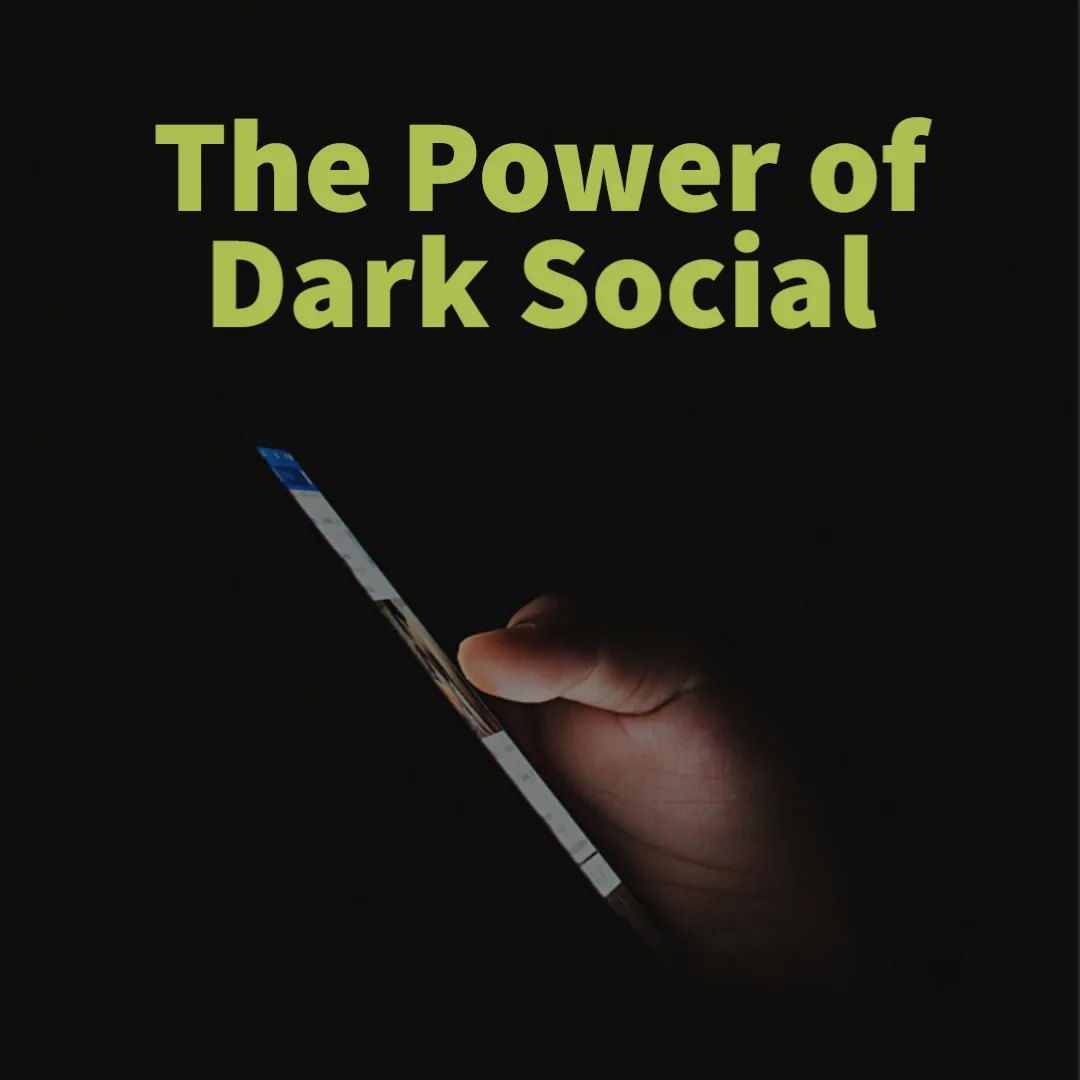 A hand holds a smartphone at an angle in a dark room, its screen glowing faintly.