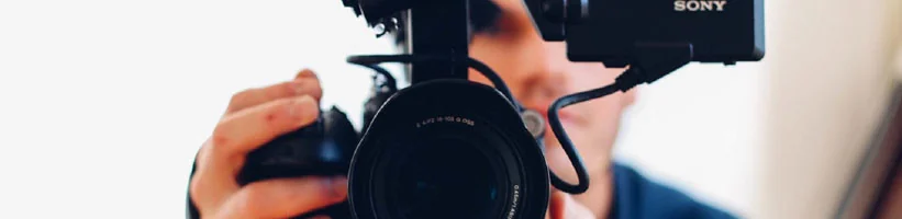 Person holding a Sony video camera up to their face, with the lens pointed at the viewer.