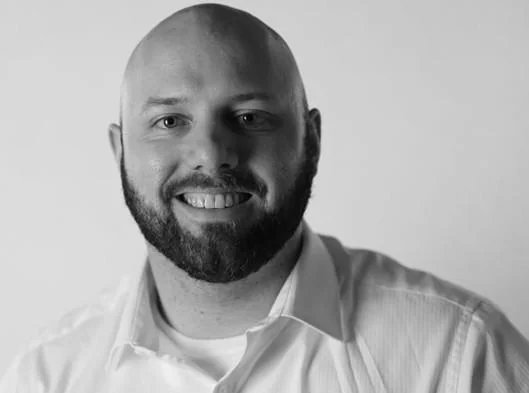 Smiling bald man with a beard wearing a white collared shirt, in black and white.