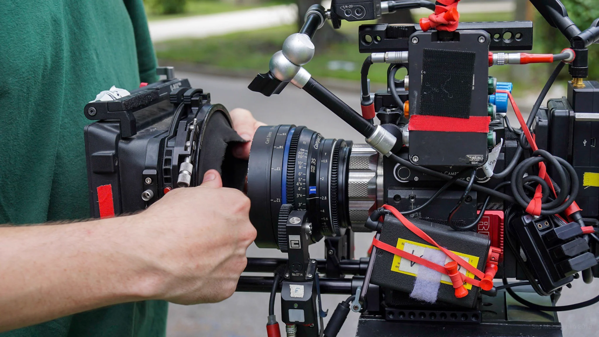 Hands adjusting the lens on a professional cinema camera rig with cables and accessories, outdoors.